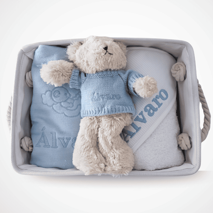 Bebé con peluche en canastilla de bebé con ropa y accesorios esenciales.